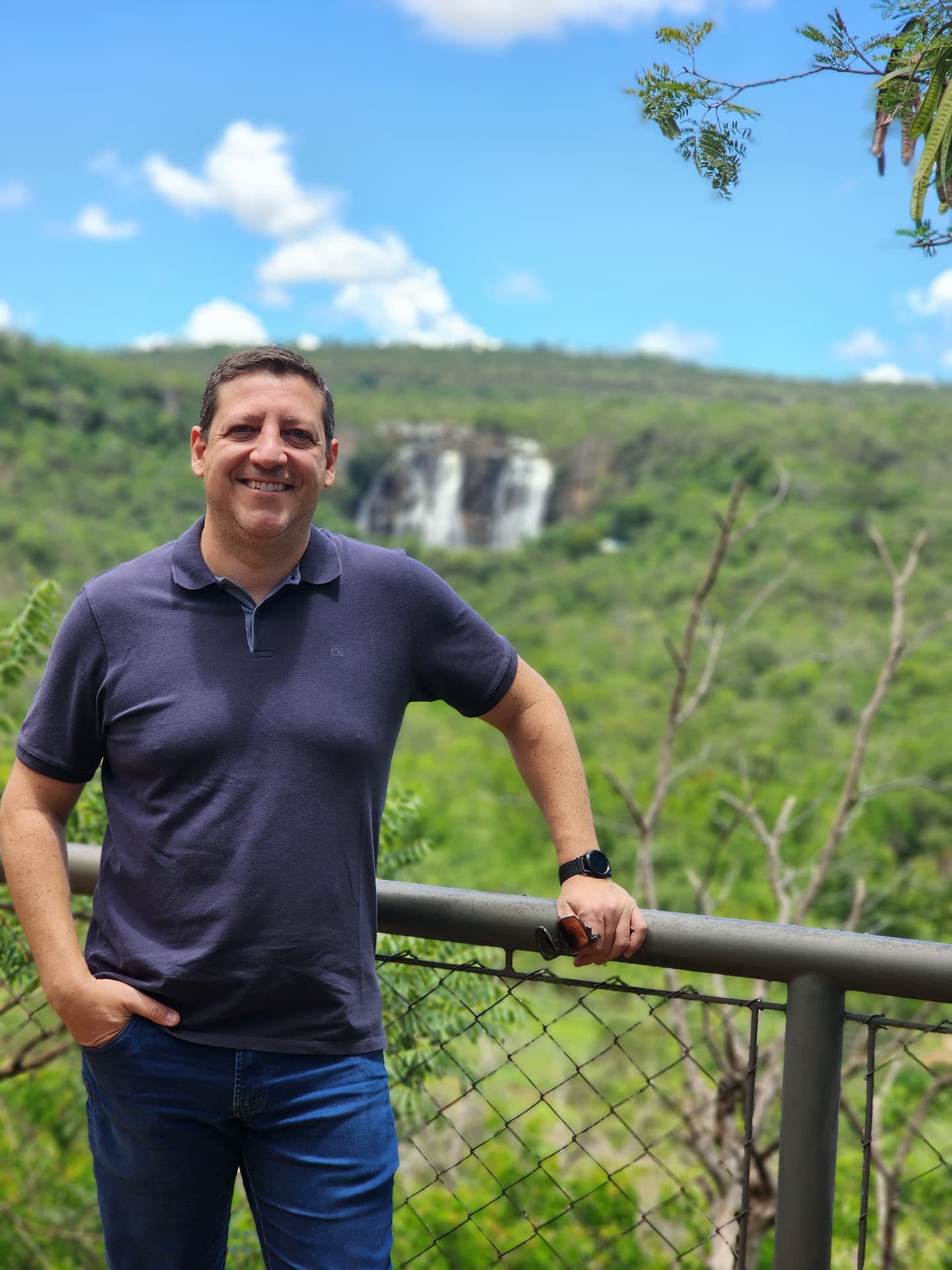 Roberio em uma trilha com cachoeira ao fundo